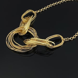 May include: A gold-toned necklace featuring a series of interconnected circular and oval links. The design consists of a delicate chain attached to a cluster of multiple overlapping rings and elongated loops, creating a layered, textured metallic appearance.
