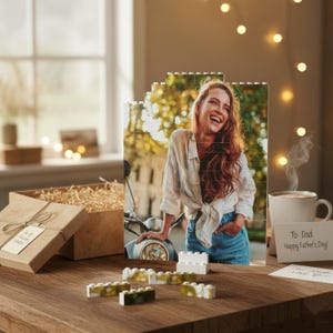 Può includere: Una foto stampata su blocchi ad incastro, raffigurante una donna sorridente. Una confezione regalo con un fiocco e un biglietto con la scritta "To Dad Happy Father's Day!" sono su un tavolo di legno. Diversi mattoncini sono sparsi intorno alla foto.