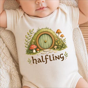 May include: Cream-colored baby onesie with a whimsical illustration of a green hobbit door set into a grassy hill, with mushrooms and the word "halfling" in brown script. The design is centered on the front of the garment.