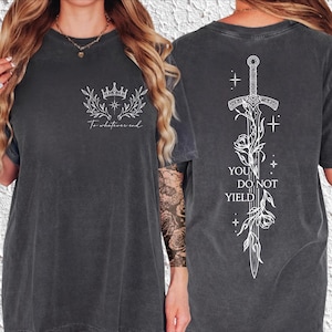 May include: A charcoal gray t-shirt featuring white line art. The front displays a crown above leafy branches and the text To whatever end. The back features a large sword entwined with floral vines, stars, and the text YOU DO NOT YIELD.