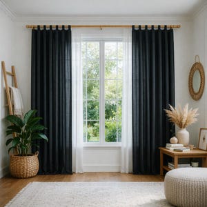 Può includere: Una stanza con una finestra incorniciata da tende nere e tende bianche trasparenti. Un'asta di legno tiene le tende. Una grande pianta in vaso si trova in un cesto intrecciato. Un tavolino di legno contiene un vaso con piante secche e una foto incorniciata.