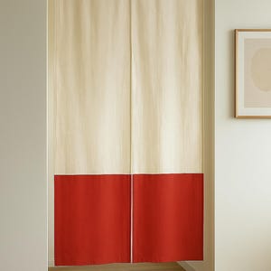 Puede incluir: Cortina de dos paneles, crema en la parte superior y roja en la inferior, colgada en una puerta. La cortina está suspendida de una barra de madera. El diseño es sencillo y moderno, adecuado para la decoración del hogar.