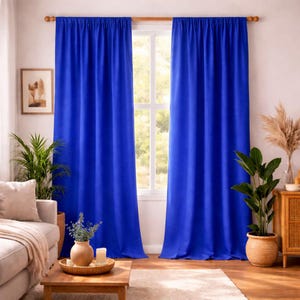Puede incluir: Cortinas azul brillante colgadas de una barra de madera, enmarcando una ventana. Las cortinas son de tela lisa y opaca. La habitación está decorada con plantas, un sofá y una mesa de madera.
