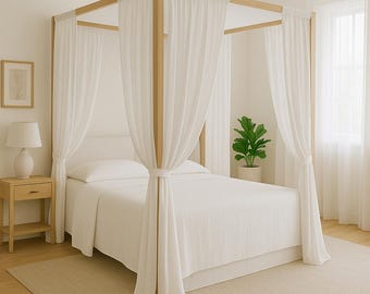 May include: A four-poster bed with a light wood frame and white sheer curtains. The bed is made with white linens and pillows. A small wooden nightstand with a lamp sits beside the bed. A potted plant is in the background.