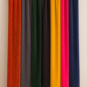 Puede incluir: Cortinas de terciopelo en varios colores, incluyendo naranja, gris, verde oscuro, negro, amarillo, rosa y azul marino. Las cortinas cuelgan de una barra negra, mostrando una gama de tonos para la decoración del hogar.