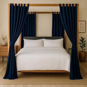 May include: A wooden four-poster bed with navy blue curtains. The bed has white bedding and pillows. A small side table with a vase and a potted plant are visible. The curtains are tied back.