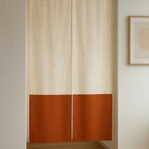 Könnte beinhalten: Ein zweiteiliger Vorhang, oben cremefarben und unten rostfarben, hängt an einer Naturholzstange. Der Vorhang befindet sich in einem Türrahmen und erzeugt eine schlichte, minimalistische Ästhetik. Das Farbschema ist neutral und warm.