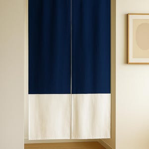Op de afbeelding: Een gordijn met twee panelen, marineblauw boven en wit onder, hangt in een deuropening. De bovenkant heeft een houten frame. De vloer is van hout. Het gordijn is verdeeld door een verticale witte naad.