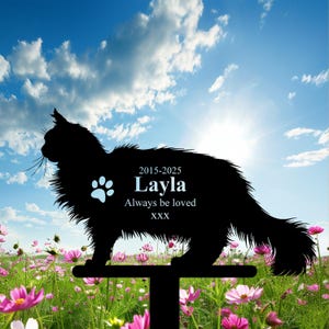 May include: A black metal cat silhouette garden stake with the name "Layla" and the text "Always be loved" and dates "2015-2025". The stake is in a field of pink flowers under a blue sky.