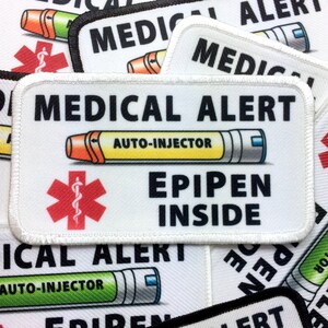 May include: White medical alert patch with black text that reads "MEDICAL ALERT" and "EPIPEN INSIDE". A red star of life with a snake wrapped around a rod is in the center of the patch. A yellow and orange auto-injector is pictured above the star of life with the text "AUTO-INJECTOR" above it.