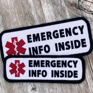 May include: Two white rectangular patches with black borders and black text that reads "EMERGENCY INFO INSIDE". Each patch features a red medical symbol with a white snake.