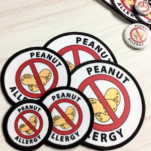 May include: Five round, white, fabric patches with black borders. Each patch has a red circle with a diagonal red line through it. The circle contains a cartoon image of peanuts. The text "PEANUT ALLERGY" is printed around the circle on each patch. The patches are in different sizes.