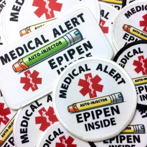 May include: A close-up of several white medical alert patches with a red star of life and the text "MEDICAL ALERT" and "EPIPEN INSIDE". The patches are made of fabric and have a white border.