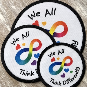 May include: Three round, white fabric patches with black trim. Each patch features a rainbow infinity symbol with hearts and the text "We All Think Differently".