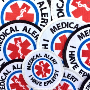 May include: A collection of white medical alert patches with a red star of life symbol and blue border. The text on the patches reads "Medical Alert", "I Have Epilepsy", and "I Have Epilepsy".