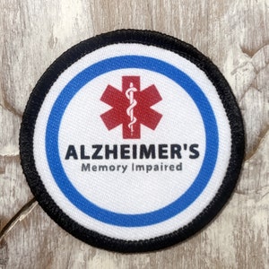 May include: A round, black-bordered patch with a blue and white circle in the center. The circle features a red medical symbol with a snake and the text "ALZHEIMER'S Memory Impaired".