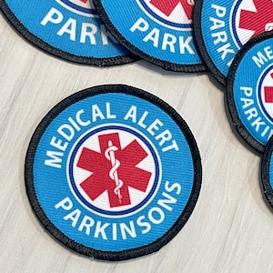May include: Blue medical alert patch with a red star of life and the text "MEDICAL ALERT PARKINSONS".