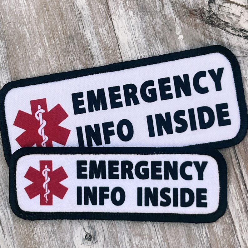 Puede incluir: Dos parches rectangulares blancos con bordes negros y texto negro que dice "Emergency Info Inside". Cada parche presenta un s&iacute;mbolo m&eacute;dico rojo con una serpiente y un bast&oacute;n.