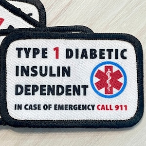May include: White patch with black border and text "TYPE 1 DIABETIC INSULIN DEPENDENT IN CASE OF EMERGENCY CALL 911". A red and blue medical symbol with a snake is in the center.