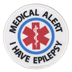 Puede incluir: Parche de alerta m&eacute;dica redondo blanco con un s&iacute;mbolo de estrella de la vida roja y el texto "MEDICAL ALERT I HAVE EPILEPSY" en negro.