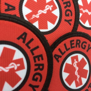 May include: Red and white allergy alert patches with a black border and the word "ALLERGY" printed in black. The patches feature a red star of life symbol with a white snake wrapped around it.