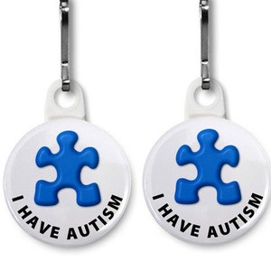 May include: Two white round Autism awareness tags with a blue puzzle piece design and the text "I HAVE AUTISM". Each tag has a silver-colored clip attached to a white plastic loop.