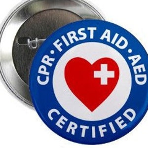 May include: A blue and white button with the text "CPR. FIRST AID. AED CERTIFIED" around a red heart with a white cross in the center.