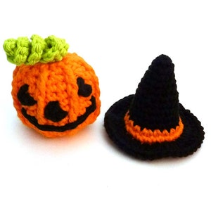 May include: Crocheted Halloween decorations featuring an orange pumpkin with a carved face and green stem, and a black witch hat with an orange brim. These handmade items are perfect for seasonal decor.