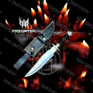 Könnte beinhalten: Ein silbernes und schwarzes Messer mit einer Lederscheide. Das Messer hat eine lange, scharfe Klinge und einen schwarzen Griff. Die Scheide ist schwarz und hat einen Schnappverschluss. Das Wort "PREDATOR" ist sichtbar.