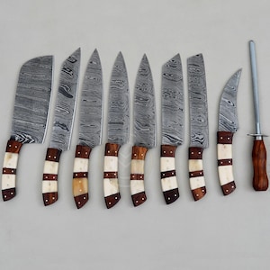 May include: A set of eight kitchen knives with Damascus steel blades and handles made of alternating segments of dark wood and light-colored bone, plus one sharpening steel with a dark wooden handle, all arranged in a row on a neutral surface.
