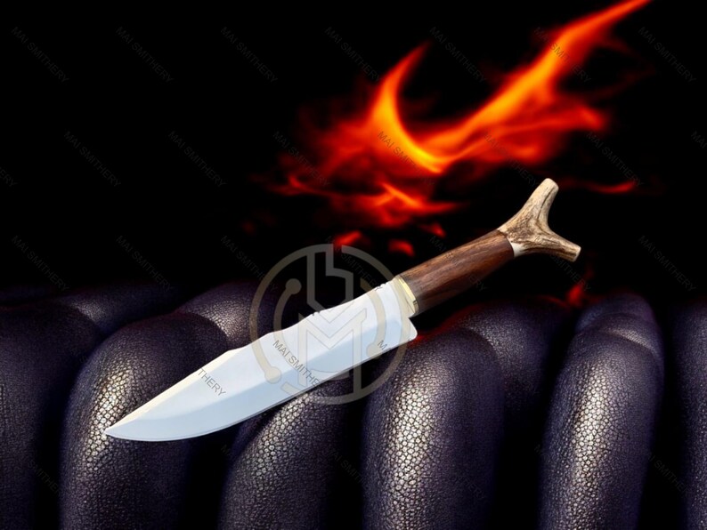 May include: A handcrafted knife with a polished steel blade and a dark wood handle. The handle features a unique antler-shaped end. The knife is set against a dark background with a fiery orange glow.