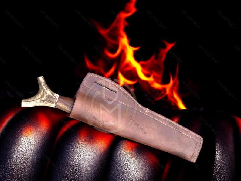 May include: A brown leather sheath with a wooden handle and a decorative antler tip. The sheath is resting on a dark, textured surface with flames in the background.