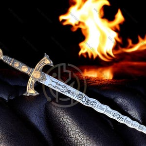 May include: An ornate dagger with a gold hilt and a silver blade, featuring engraved details and the names "Killian Jones" and "Emma Swan". The handle has a red gem. A fiery background adds drama.