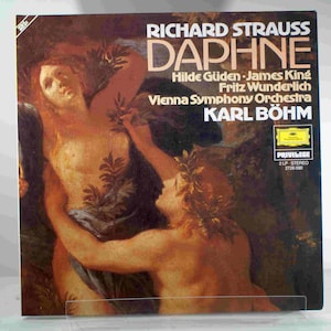 May include: A vintage vinyl record cover for Richard Strauss's Daphne, featuring a painting of two nude figures embracing in a lush forest setting. The cover includes the title "Daphne", the composer's name "Richard Strauss", the performers' names "Hilde Güden, James King, Fritz Wunderlich", the orchestra "Vienna Symphony Orchestra", the conductor "Karl Böhm", and the record label "Privilege".