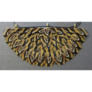 May include: A necklace featuring a fan-shaped pendant made of brown, black, and white feathers. The feathers are attached to a dark blue cord with gold-colored metal accents. The pendant has a natural, organic appearance.