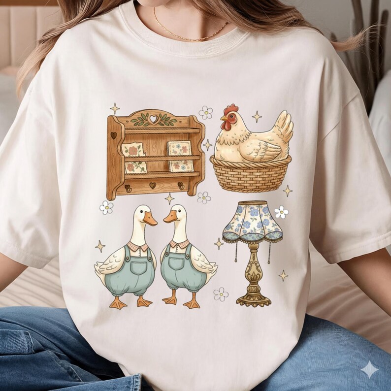 May include: Cream-colored t-shirt featuring a whimsical illustration of a wooden shelf, a hen in a basket, two ducks in overalls, and a floral lamp. The design has a vintage, farmhouse aesthetic with soft colors and charming details.