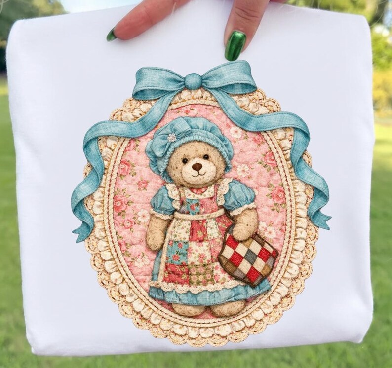 May include: White t-shirt with a teddy bear illustration. The bear is dressed in a blue bonnet and dress, carrying a checkered bag. The design is framed by a blue ribbon and an oval border.