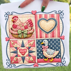 May include: White square fabric with a patchwork design featuring a chicken in a basket, a heart, a star, and a duck. The design incorporates floral patterns, stripes, and polka dots in pink, red, blue, and green. The border is a dark blue with decorative swirls and hearts.