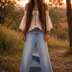 Könnte beinhalten: Eine Frau trägt ein weißes schulterfreies Spitzentop und einen langen Jeansrock mit einem Frontpanel-Design. Sie trägt eine Gürtelschnalle mit Friedenszeichen und einen Blumenkranz. Der Hintergrund ist eine verschwommene Szene im Freien.