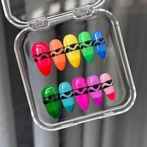 May include: A set of ten almond-shaped press-on nails arranged in a clear plastic case. Each nail features a vibrant, multi-coloured design resembling a crayon, with a black wavy line detail across the centre and a solid coloured tip.