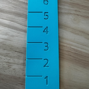 May include: A bright turquoise ruler with measurements from 1 to 6 inches. The numbers and markings are etched into the ruler's surface. The ruler is rectangular with rounded corners.