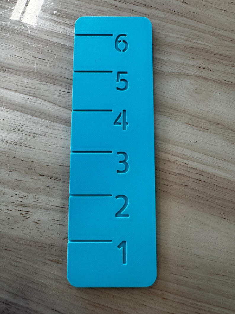 May include: A bright turquoise ruler with measurements from 1 to 6 inches. The numbers and markings are etched into the ruler's surface. The ruler is rectangular with rounded corners.