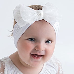 Pu&ograve; includere: Un cerchietto bianco con un fiocco di tulle bianco. Il cerchietto &egrave; indossato da un bambino con occhi azzurri e un grande sorriso.