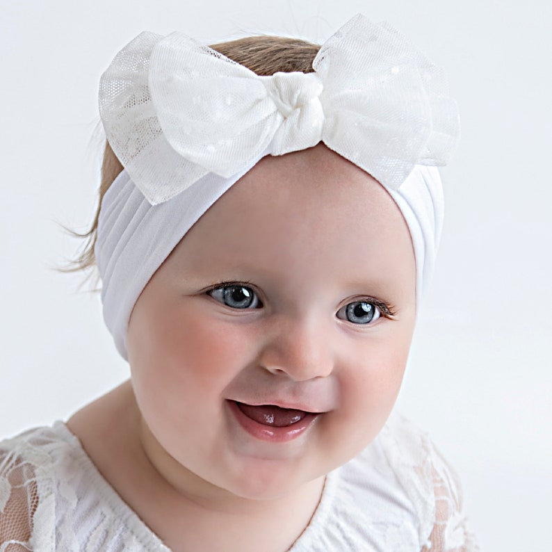Pu&ograve; includere: Un cerchietto bianco con un fiocco di tulle bianco. Il cerchietto &egrave; indossato da un bambino con occhi azzurri e un grande sorriso.