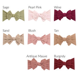 May include: A collection of eight ribbed fabric headbands in various colors, including sage, pearl pink, wine, sand, blush, tan, antique mauve, and burgundy. Each headband features a large bow.