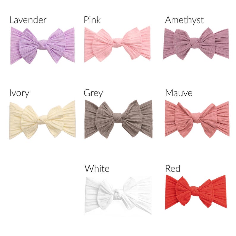 May include: A collection of eight ribbed fabric headbands in various colors, including lavender, pink, amethyst, ivory, grey, mauve, white, and red. Each headband features a large bow design.
