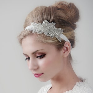 Pu&ograve; includere: Un cerchietto bianco con un design floreale argentato decorato con strass. Il cerchietto &egrave; indossato da una donna con i capelli raccolti in uno chignon.