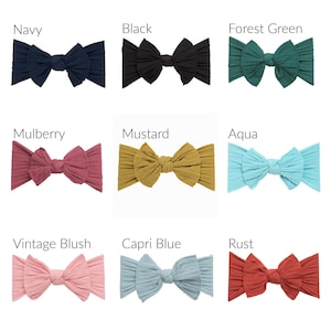 May include: Nine different ribbed fabric headbands in various colors are displayed. Colors include navy, black, forest green, mulberry, mustard, aqua, vintage blush, capri blue, and rust. Each headband is tied in a bow.