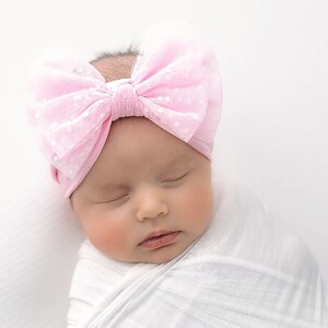 Pu&ograve; includere: Un cerchietto rosa a pois con un grande fiocco in cima. Il cerchietto &egrave; indossato da un bambino che dorme in un fasciatoio bianco.