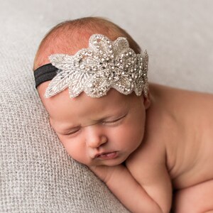 Pu&ograve; includere: Una bambina addormentata che indossa una fascia per capelli argentata e bianca con strass. La fascia &egrave; su un elastico nero.
